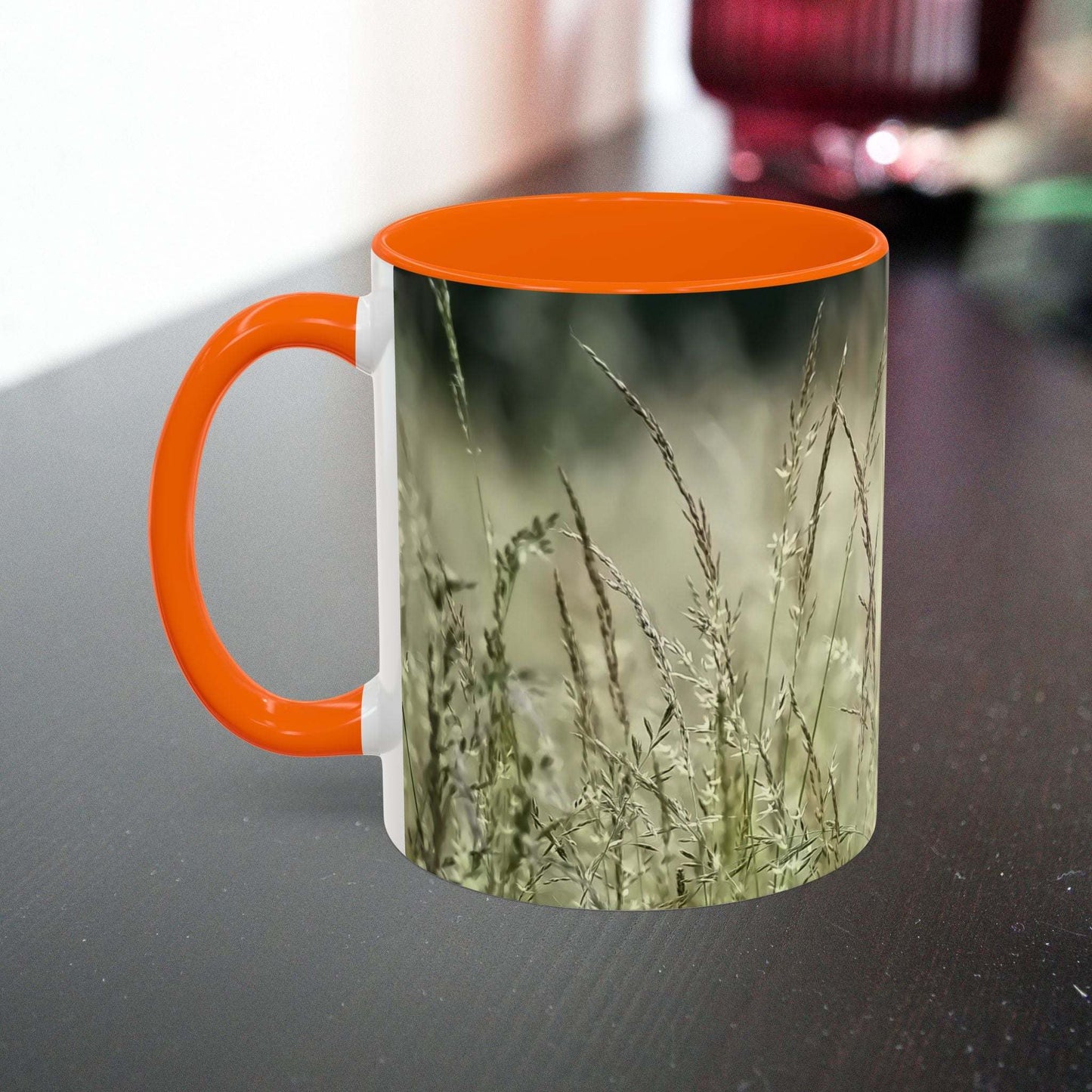 Ceramic mug with flowering grass design and orange handle.