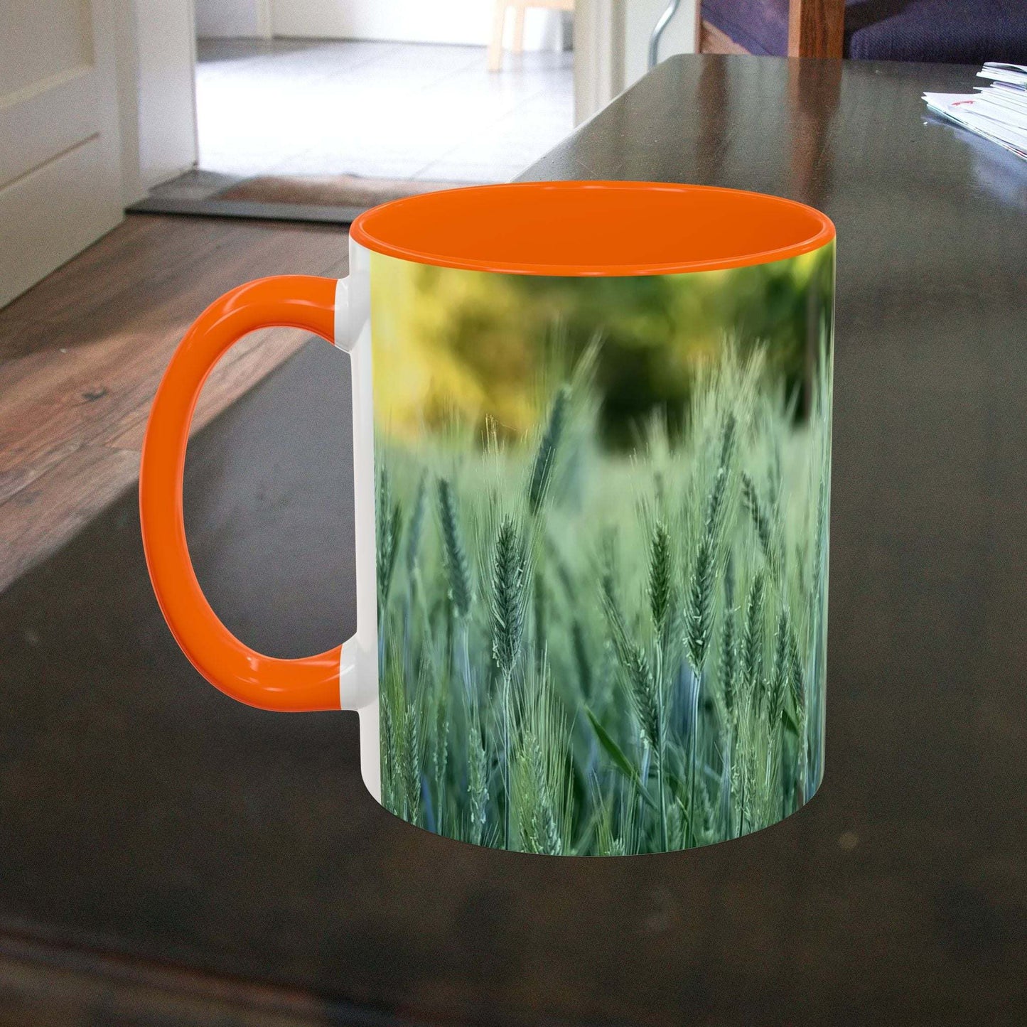 Wheat field design coffee mug with orange handle on a table.