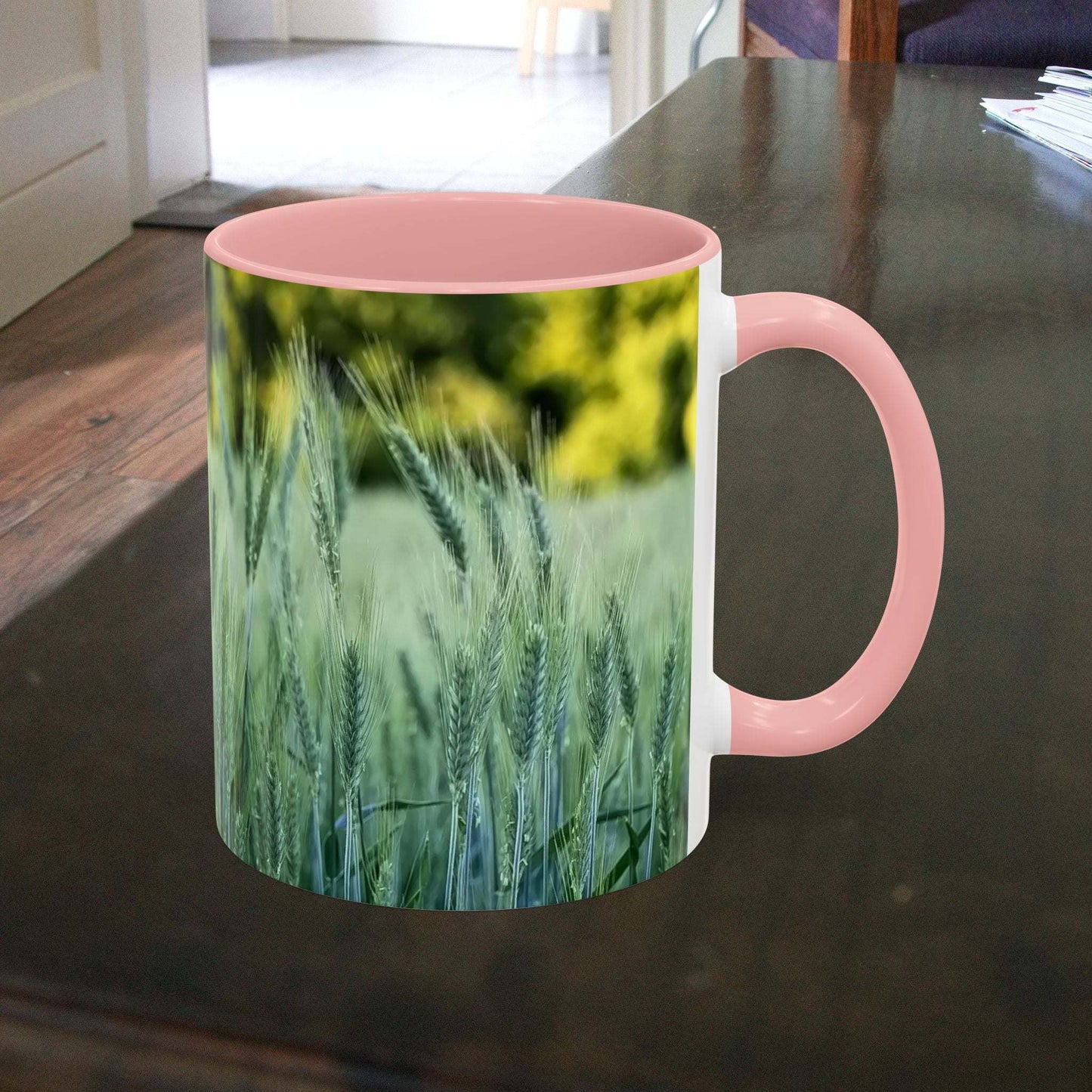 Wheat field design coffee mug with pink handle on table.