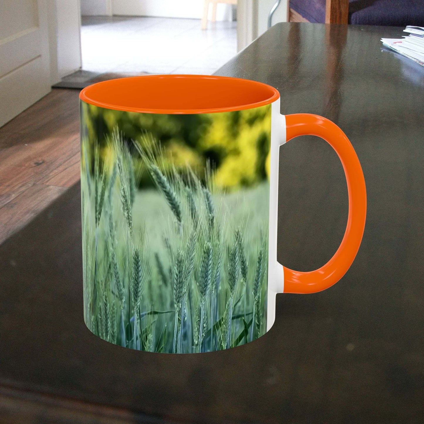 Wheat field design coffee mug with orange handle on a dark table.