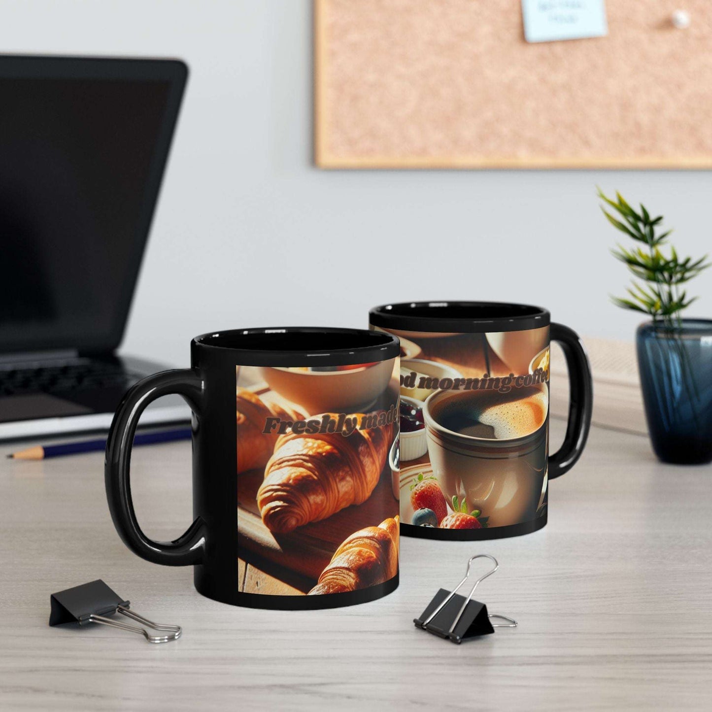 Black coffee mug with "Freshly Made Good Morning Coffee" design, available in 11oz and 15oz sizes, on a desk setting with plants and office supplies.