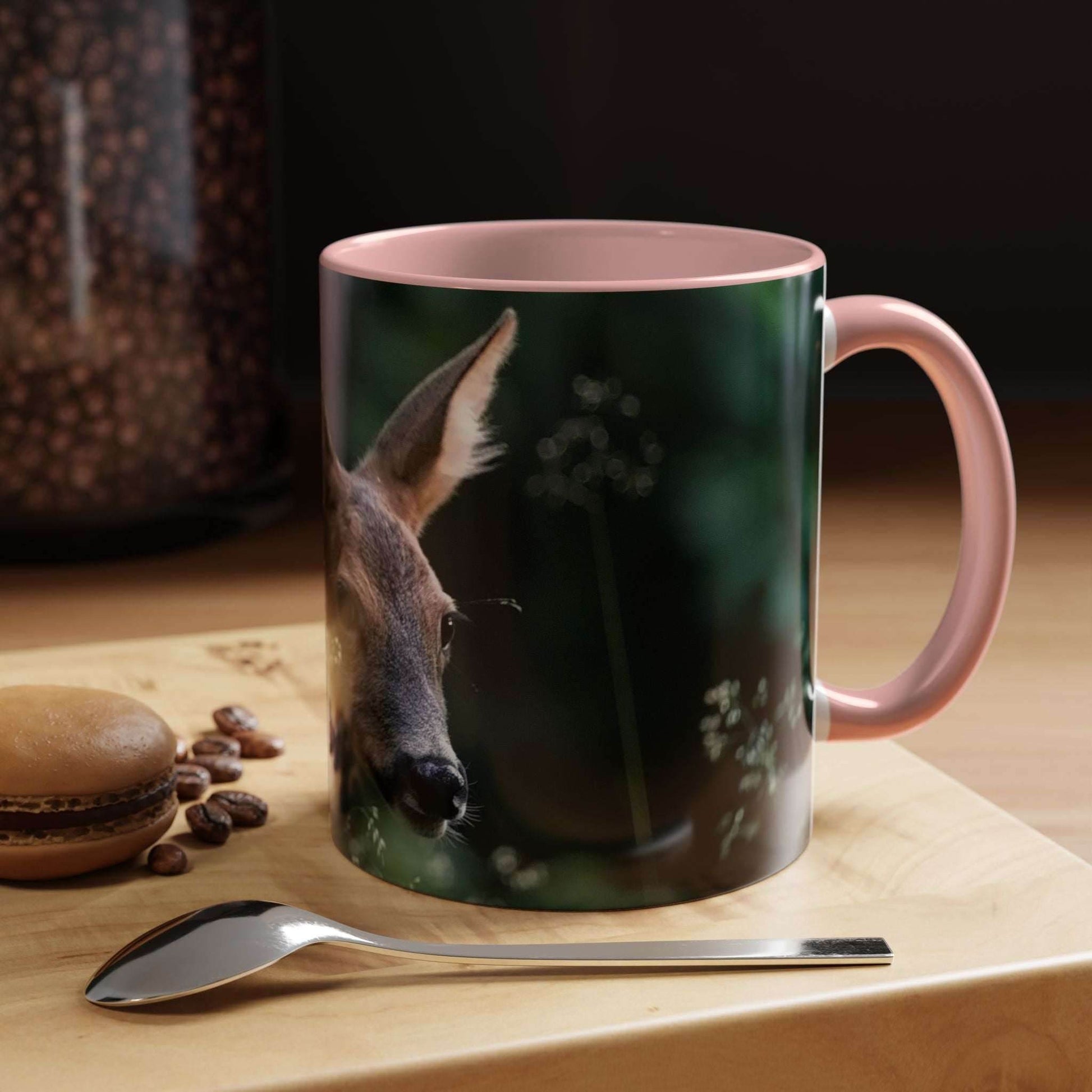 Nature-inspired deer ceramic mug with floral accents, 11oz size, pink handle, placed beside coffee beans and macarons.