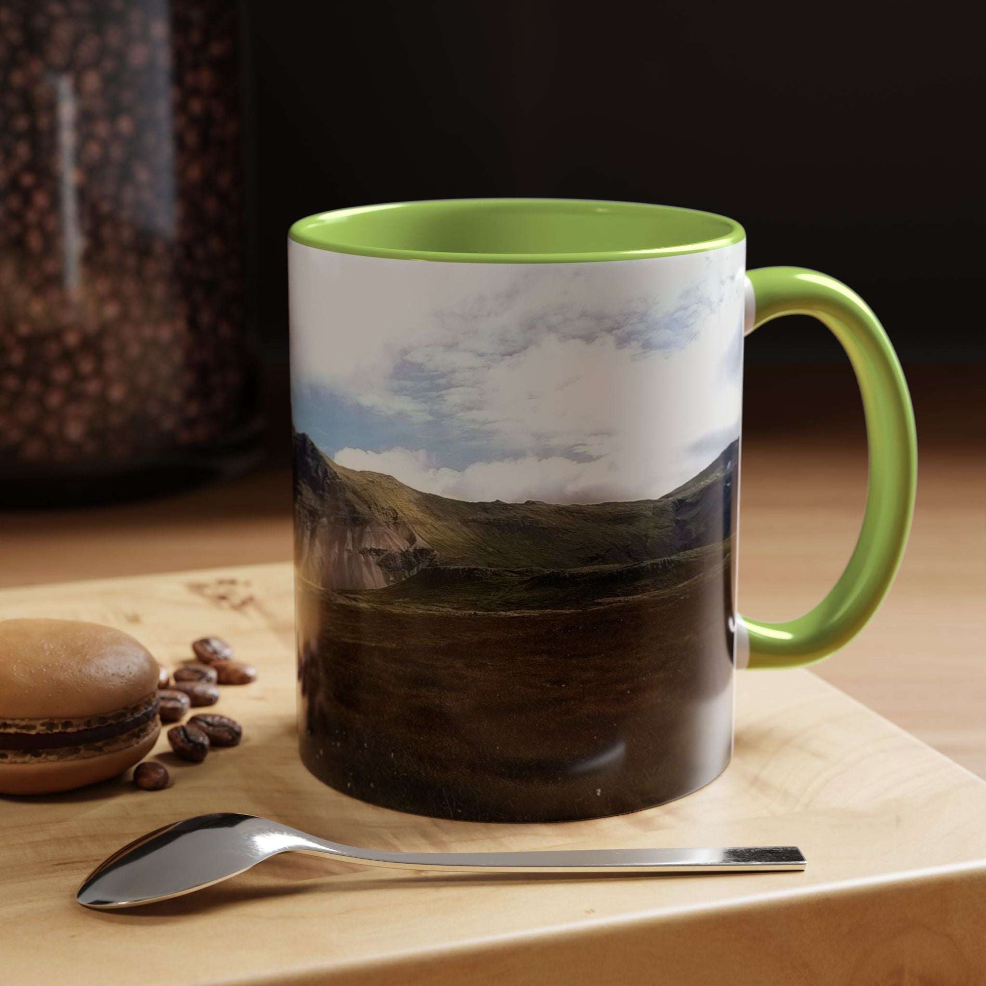 Iceland scenery coffee mug with vibrant colors on wooden table with macaron and spoon.