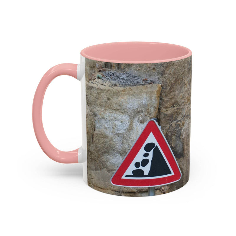 Adventurous 11oz Rocky Mug, Mountain Lovers, Danger of Falling Rocks with a pink handle and pink inside on a bright surface.
