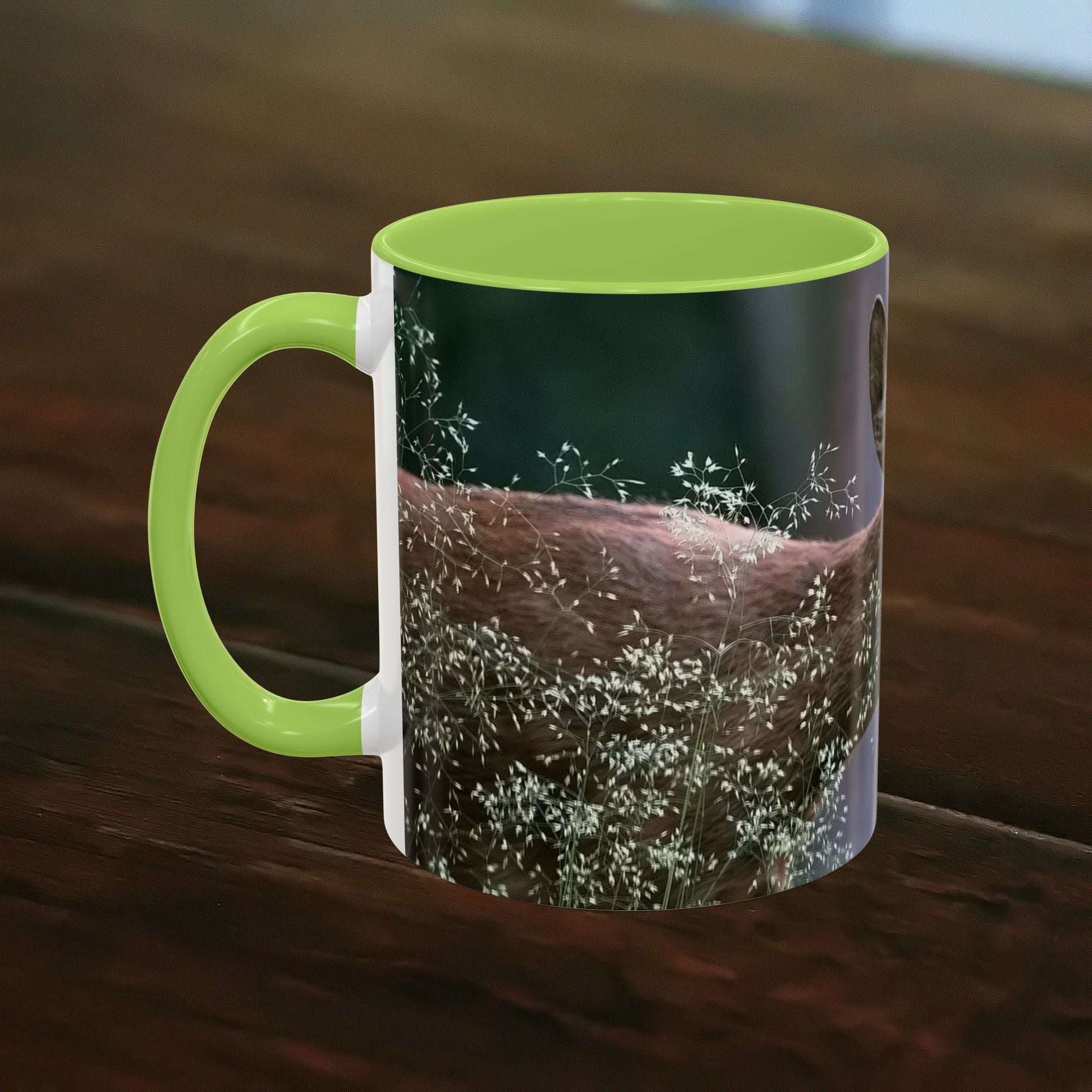 Mug with nature-inspired deer and floral print, green handle, and rim on dark wood surface.