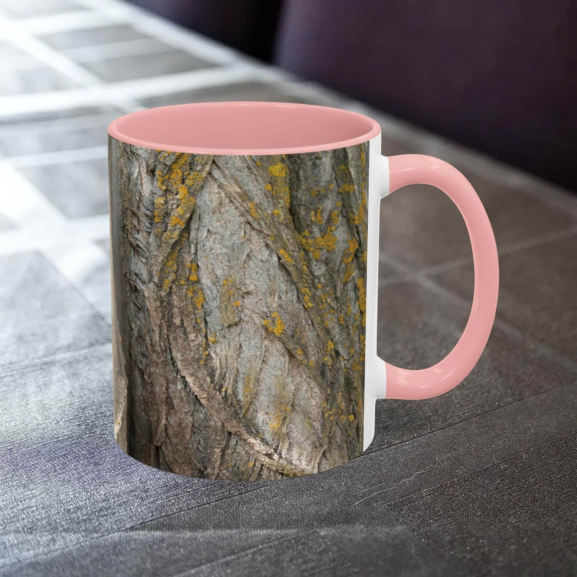Coffee mug with a tree trunk design and pink handle on a table.